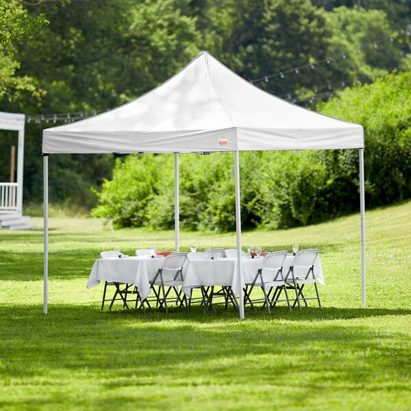 A white Galaxy Equipment 10' x 10' canopy with tables and chairs on grass.