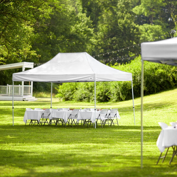 A white Backyard Pro canopy set up in a grassy area with tables and chairs.