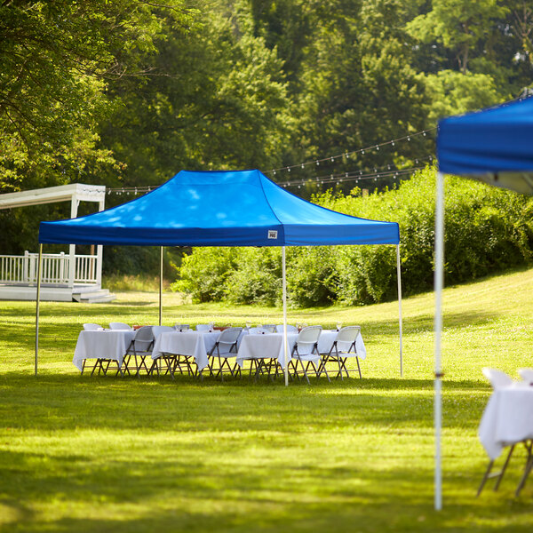 A blue Backyard Pro canopy set up over tables and chairs in a grassy area.