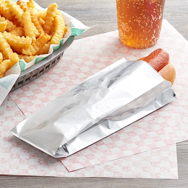 A hot dog in a Carnival King foil wrapper next to a basket of fries.