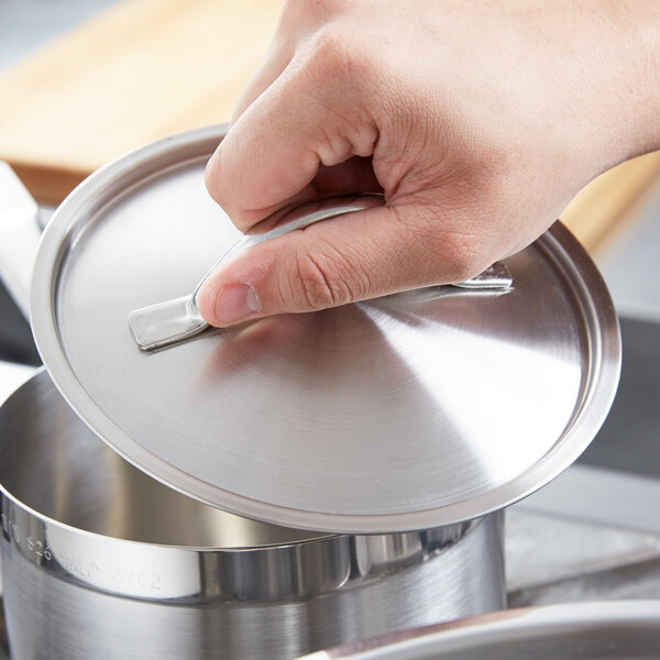 A person holding a Vollrath stainless steel domed lid over a pot.