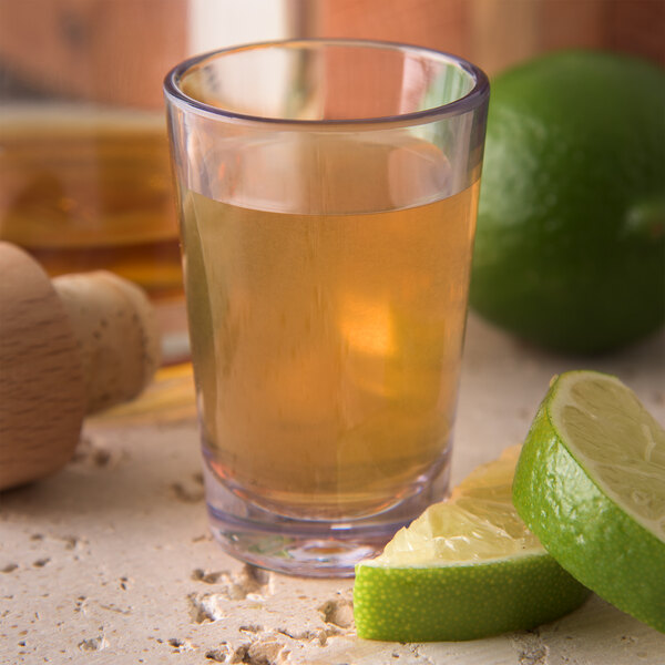 A Carlisle SAN plastic dessert shot glass filled with a drink and limes.