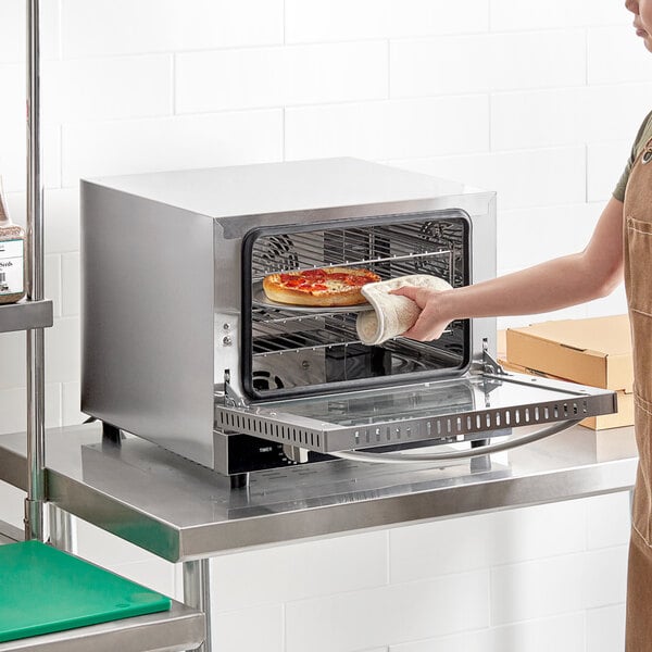 A woman in an apron putting pizza in a Galaxy countertop convection oven.