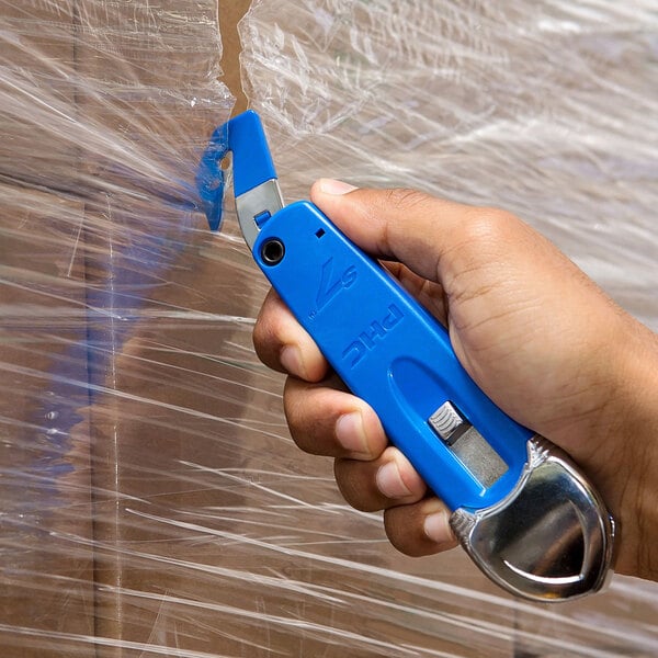 A hand holding a blue Pacific Handy Cutter to cut plastic.