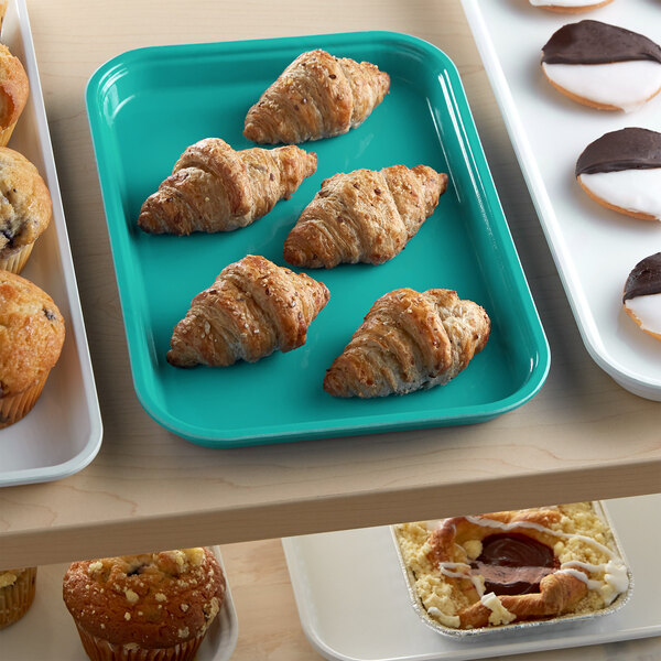 A green Cambro market tray filled with pastries and muffins on a table.
