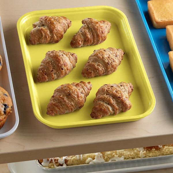 A yellow Cambro market tray with croissants and pastries on it.