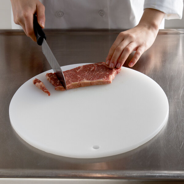A chef using a Thunder Group round white cutting board to cut meat.