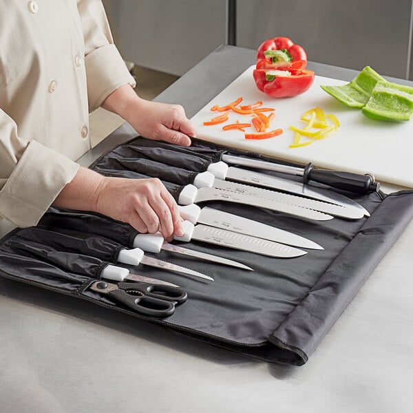 A woman using a Choice 11 piece knife set with white handles to cut vegetables on a cutting board.