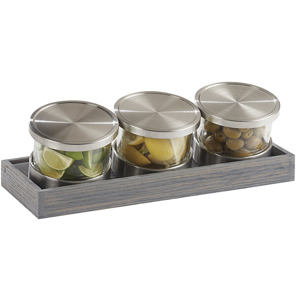 A Cal-Mil Ashwood tray with three glass jars and metal lids filled with limes.