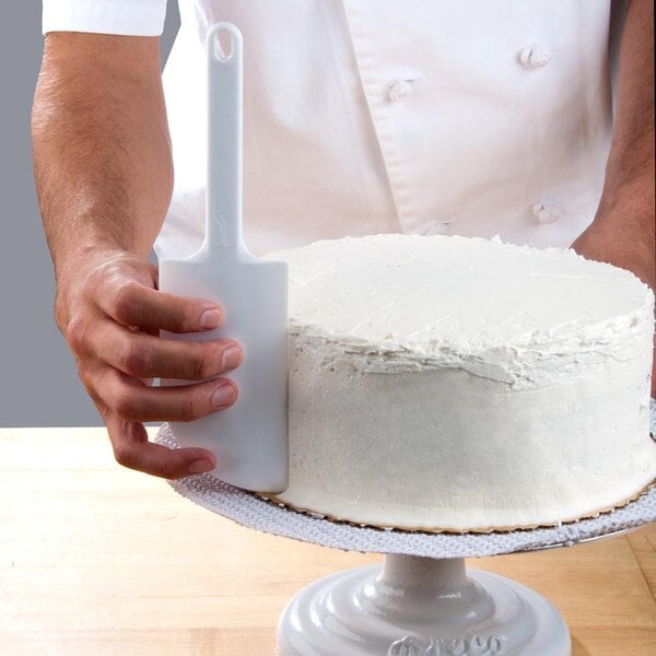 A person holding an Ateco baking / icing spatula with a white cake.