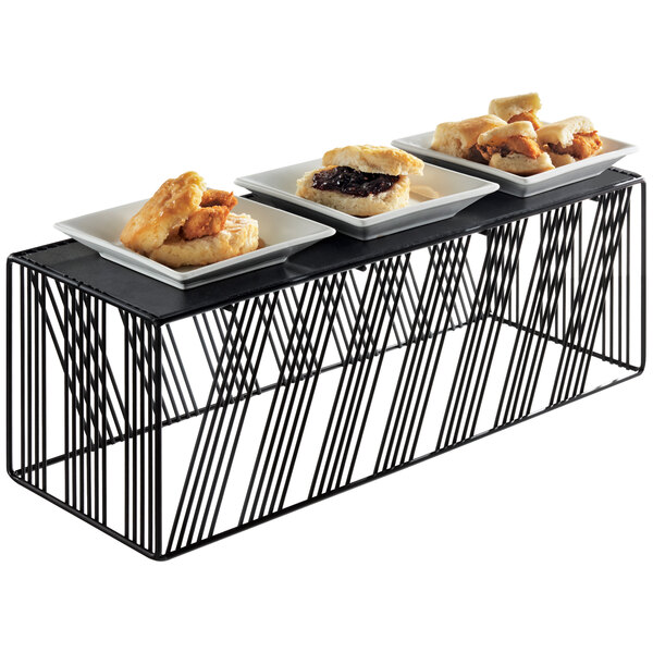 A black Cal-Mil rectangular riser holding plates of food on a table.