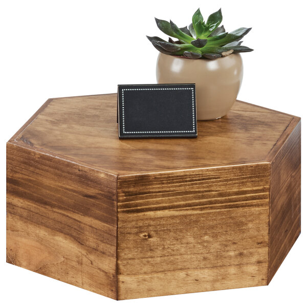 A Cal-Mil oak wood hexagon riser holding a brown pot with a succulent plant on a wooden table.