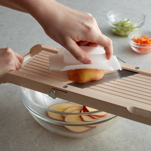 A person using a Benriner Japanese mandoline to slice apples.