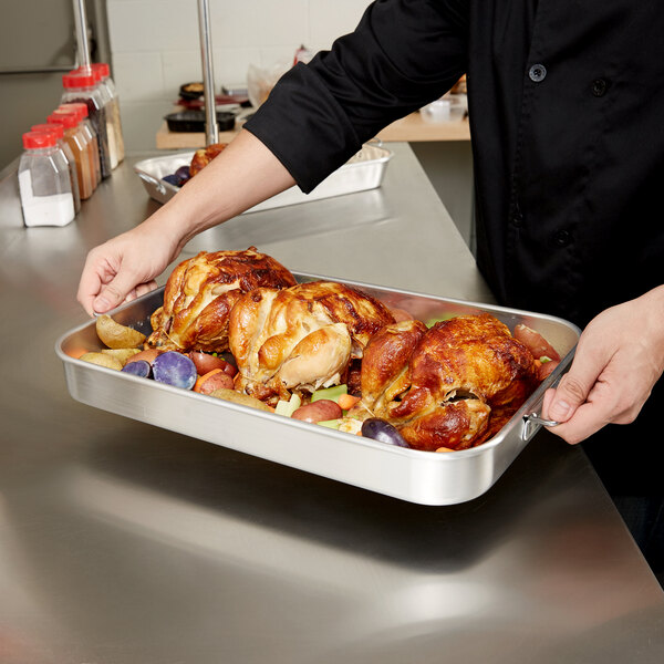 A chef holding a Vollrath aluminum baking and roasting pan with handles full of cooked turkey.