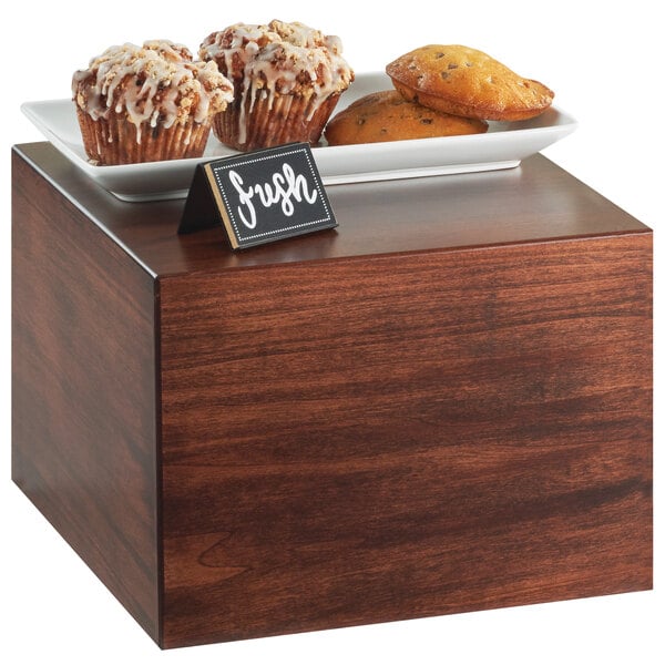 A wooden square riser with muffins and cookies on it.