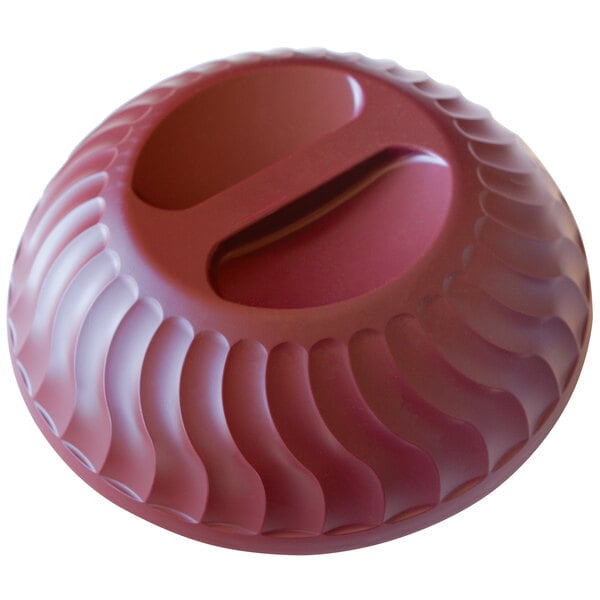 A red circular plastic dome with a wavy design over a hole.