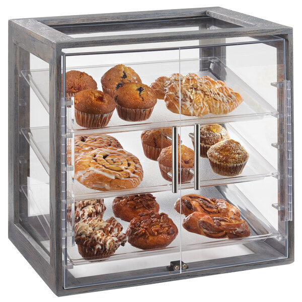A Cal-Mil Ashwood Gray Oak acrylic display case with 3 trays of muffins, cinnamon rolls, and pecans.
