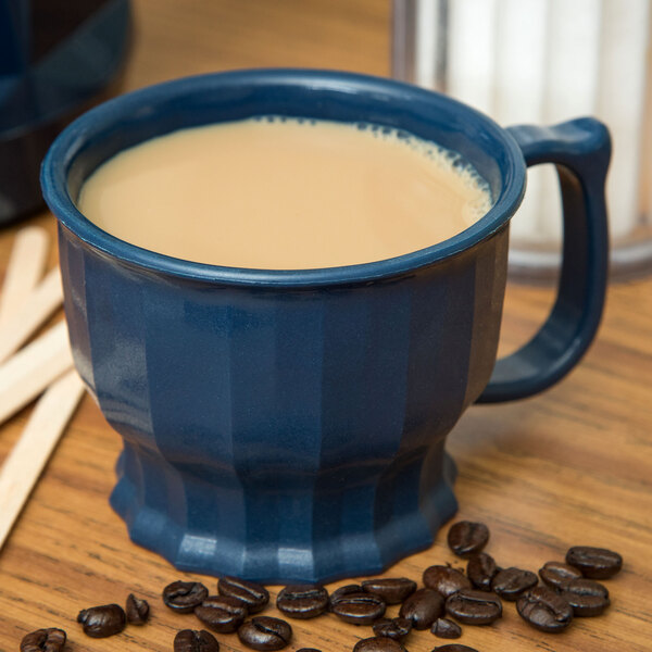 A dark blue Dinex Tropez mug filled with a brown liquid on a counter next to coffee beans.