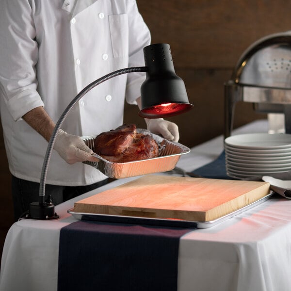 A chef using an Avantco countertop bulb warmer to keep meat warm on a table.