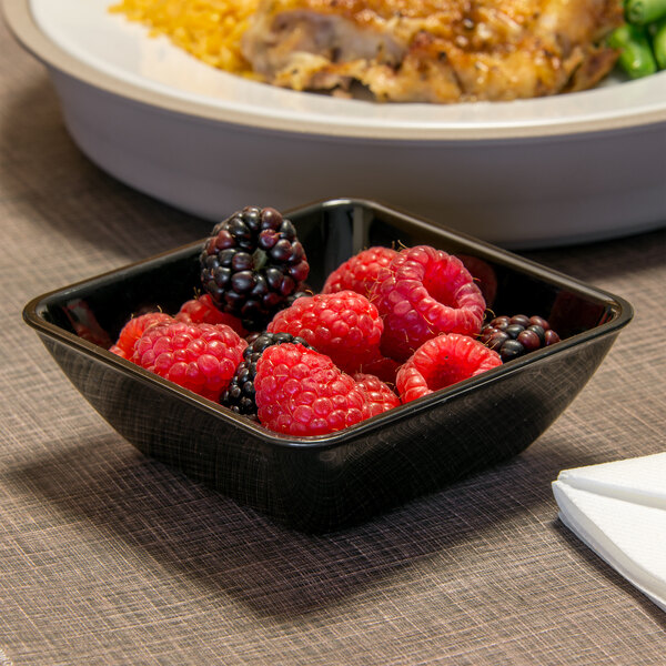 A Dinex black SAN plastic bowl filled with raspberries and blackberries on a table next to a plate of food.