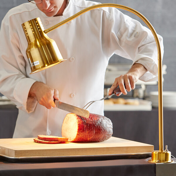 A chef cutting a piece of meat with a gold Avantco heat lamp.
