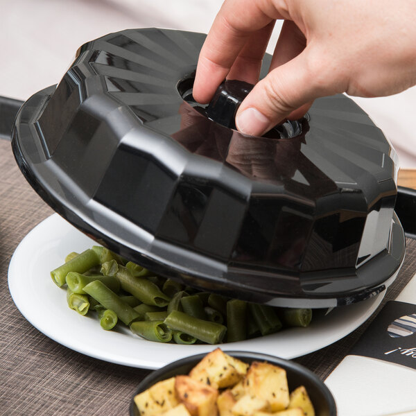 A hand using a black Dinex convection dome to cover a plate of food.