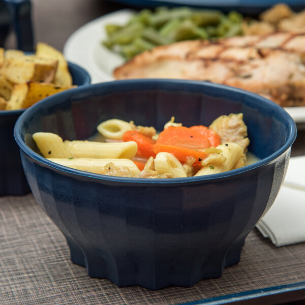 A close up of a blue Dinex bowl with pasta, carrots, and a piece of food.