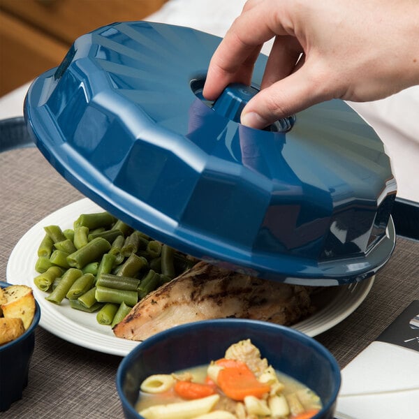 A person holding a Dinex dark blue convection dome over a plate of food.