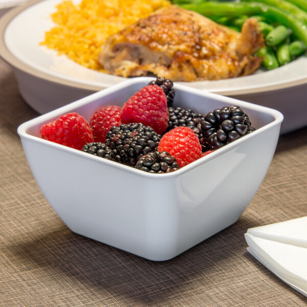 A white Dinex square plastic bowl filled with berries on a table.
