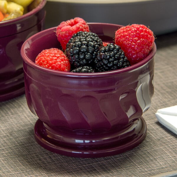 A bowl of cranberries sits on a table next to a bowl of fruit.
