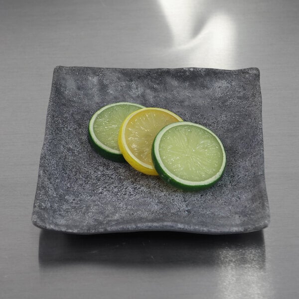A Elite Global Solutions coal square melamine plate with slices of lemon and lime on it.