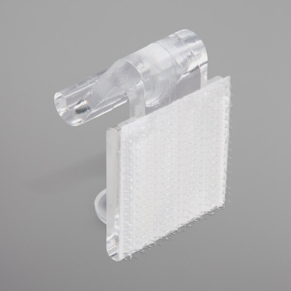 A close-up of a clear plastic Snap Drape table skirt clip with a white plastic strip attachment.