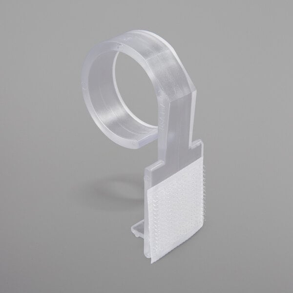 A clear plastic table skirt clip with a white hook and loop attachment.