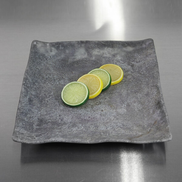 An Elite Global Solutions Basalt square melamine plate with slices of lemon and lime on it.