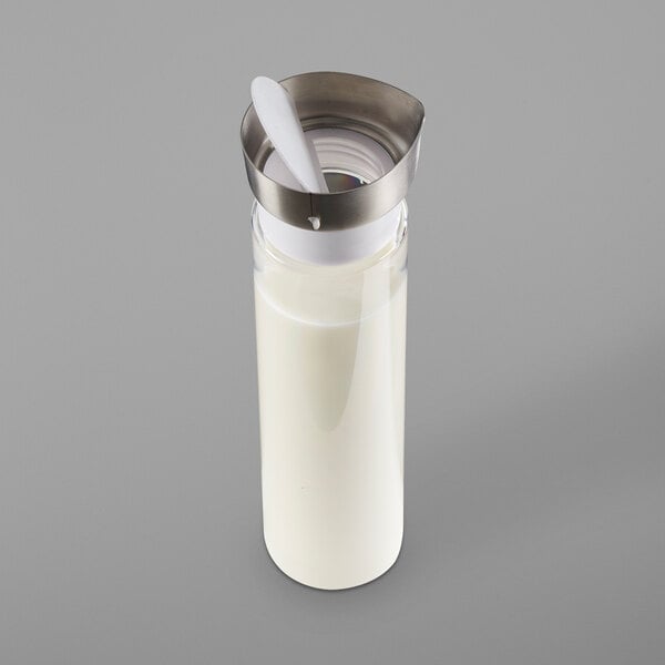 A Cal-Mil polycarbonate carafe with a hinged closing lid filled with milk and a spoon inside.