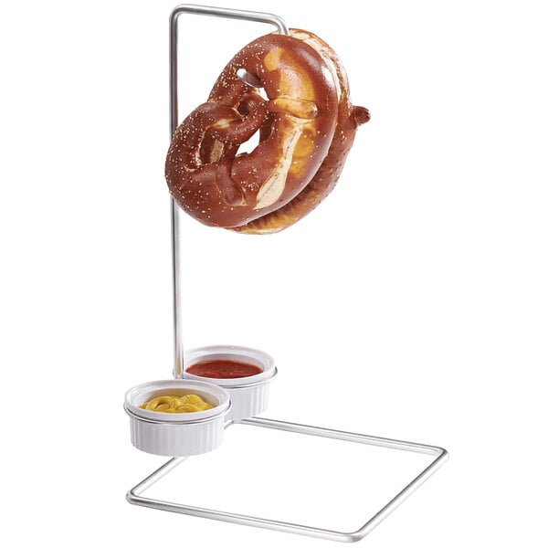 A Cal-Mil wire double pretzel holder with 2 ramekins holding a pretzel and dipping sauce.