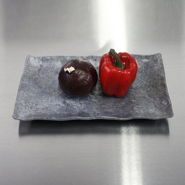 An Elite Global Solutions rectangular coal melamine plate with a red pepper and a black onion on it.