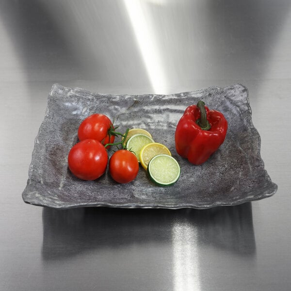 A rectangular coal melamine bowl filled with tomatoes, peppers, and limes.