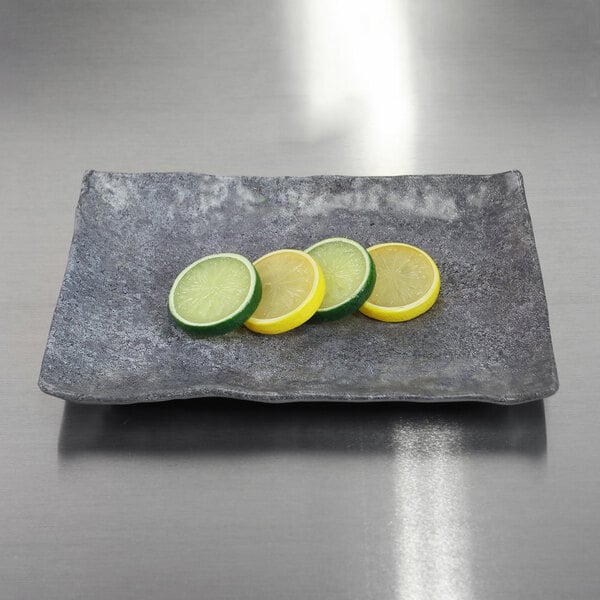 An Elite Global Solutions Basalt rectangular melamine plate with slices of lemons and limes on it.