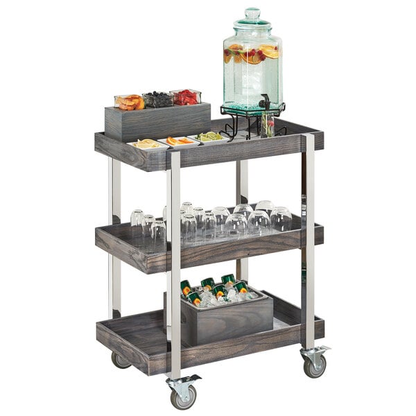 A Cal-Mil Ashwood Gray Oak wooden serving cart with drinks and glasses on it.