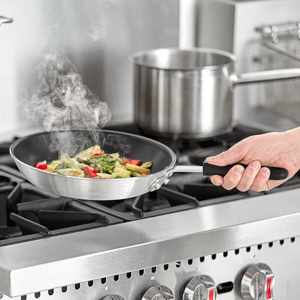 A hand holding a Choice aluminum non-stick fry pan with food cooking in it.
