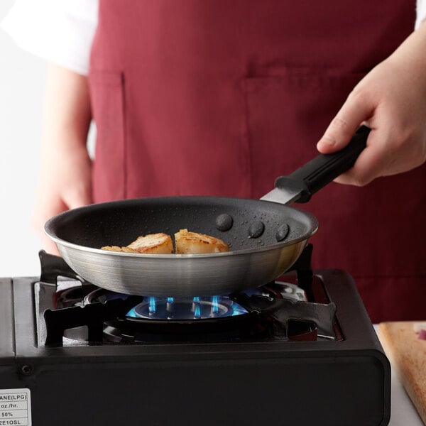 A person cooking scallops in a Choice aluminum non-stick fry pan on a stove.