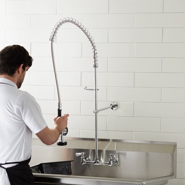 A man in a white shirt and black apron using a Chrome-Plated Wall-Mount Pre-Rinse Faucet.