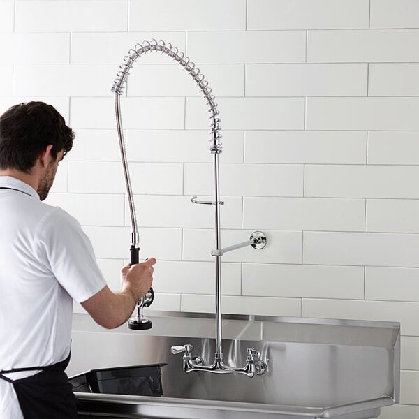 A man in a white shirt and black apron using a Regency wall mount pre-rinse faucet over a sink in a professional kitchen.