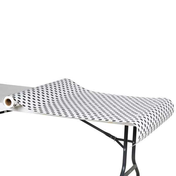 A roll of black and white polka dot wrapping paper on a table with a black and white polka dot table cover.