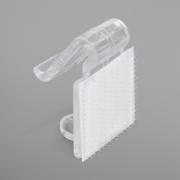 A close-up of a Snap Drape clear plastic table skirt clip with a white plastic strip attached.