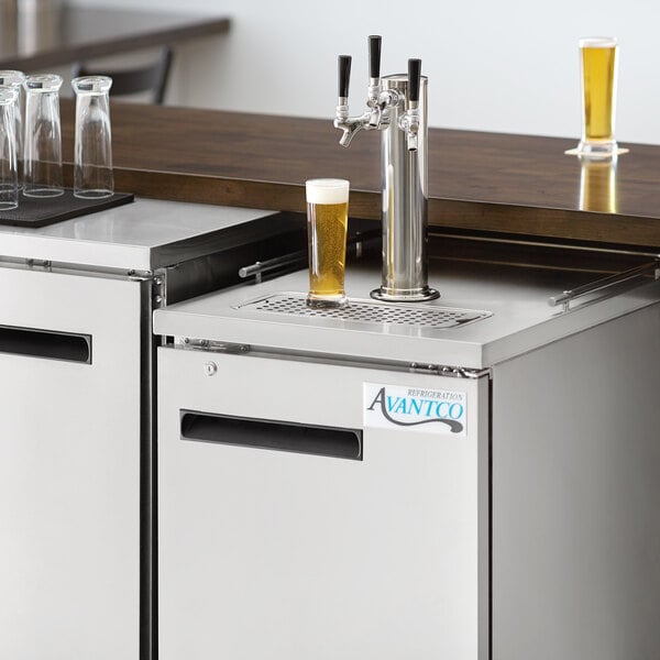 An Avantco stainless steel beer dispenser on a counter with two beer taps and a glass being filled with beer.
