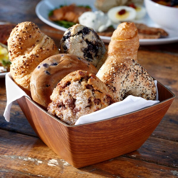 A square faux wood bowl filled with assorted pastries on a table.