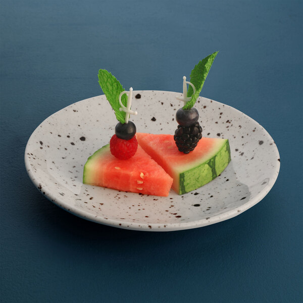 A slice of watermelon with a raspberry on a chocolate chip round melamine plate with fruit.