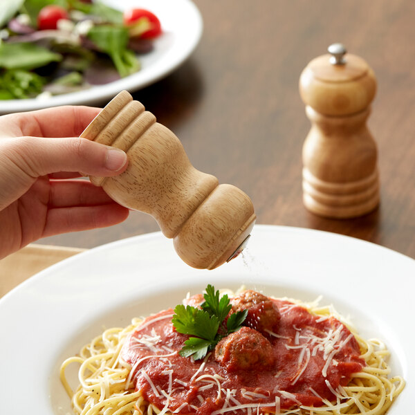 A hand holding an Acopa wooden pepper shaker over a plate of spaghetti.